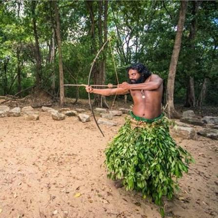 A Vedda man in traditional leaf attire draws a hunting bow near Dambana, Sri Lanka