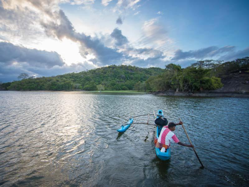 A local paddler in a small outrigger boat on Sorabora Wewa reservoir at dusk, Sri Lanka